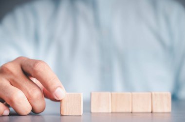 Mavi gömlekli bir iş adamı, boş tahta blokları elleriyle düzenliyor. Beyaz ahşap bir masanın üzerine yerleştirilmiş. İş stratejisi ve eylem planı. Boşluğu kopyala.