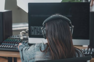 Masada oturan bir kadın şarkıcı kaydını kontrol ediyor. Masanın üzerinde bir kayıt cihazı var..