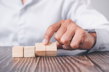 Mavi gömlekli bir iş adamı, boş tahta blokları elleriyle düzenliyor. Beyaz ahşap bir masanın üzerine yerleştirilmiş. İş stratejisi ve eylem planı. Boşluğu kopyala.