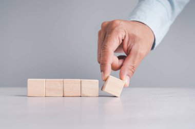 Mavi gömlekli bir iş adamı, boş tahta blokları elleriyle düzenliyor. Beyaz ahşap bir masanın üzerine yerleştirilmiş. İş stratejisi ve eylem planı. Boşluğu kopyala.