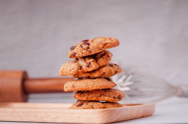 Piles of delicious chocolate chip cookies on a white plate with a milk bottle. Pastry utensils with white linen napkins on a wooden table. Delicious on a white plate with a bottle of milk.
