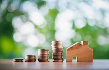 Masa başında ahşap bir evi olan bozuk para yığını. Emlak yatırım işleri için finansal strateji fikirleri. Doğal yeşil geçmişi olan..