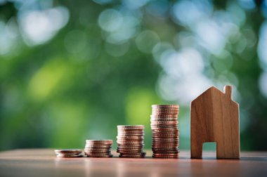 Masa başında ahşap bir evi olan bozuk para yığını. Emlak yatırım işleri için finansal strateji fikirleri. Doğal yeşil geçmişi olan..