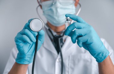 Doktorlar cerrahi maske ve gözlük takıyor, bilim adamları COVID-19 için şırınga ve aşı tutuyor. Aşı ve laboratuvar deneyleri. Virüs koruma kavramı COVID-19.