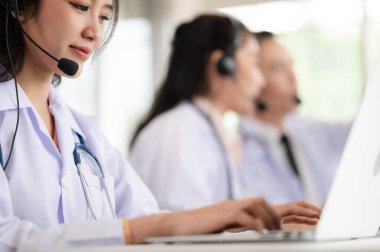 Asya sağlık ekibi çevrimiçi sağlık tavsiyesi veriyor. Gülümseyen yüz, kliniklerde mikrofon ve steteskopla kulaklık takarak ayakta duruyordu. Uzaktan tedavi kavramı, sağlık hizmetleri çağrı merkezi çevrimiçi..
