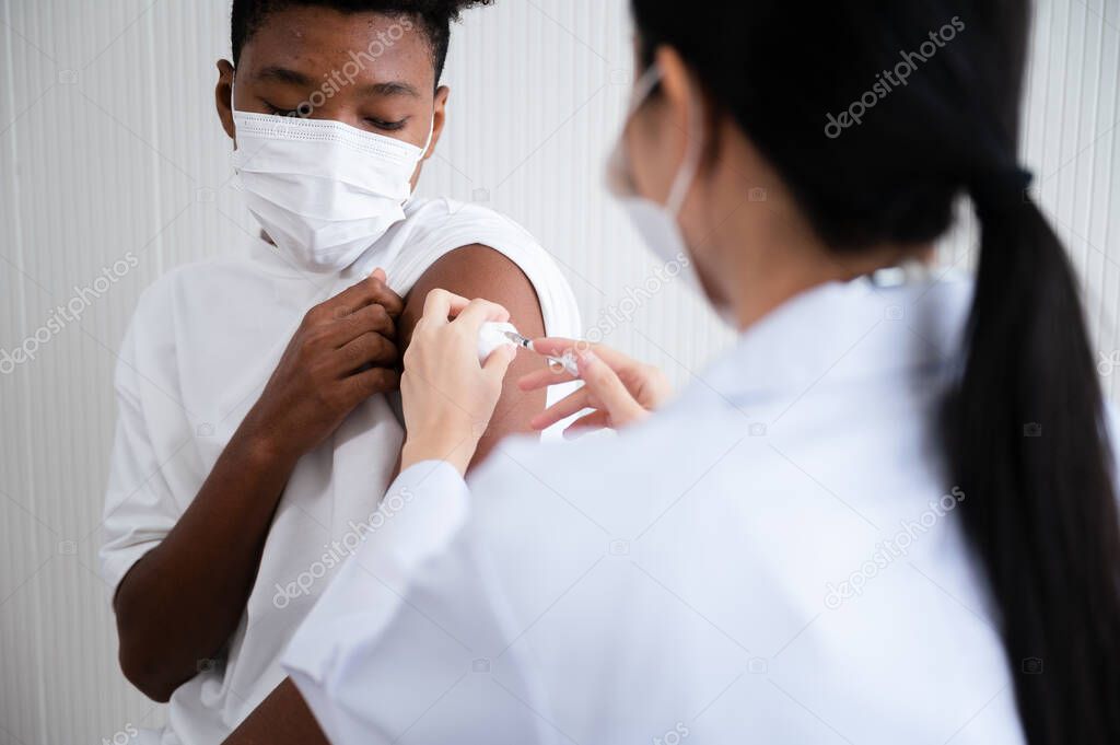Female doctor or nurse vaccinating against coronavirus 19 at the shoulders African-American man. By wearing a mask at all times. Concept of preventing the spread of COVID-19.