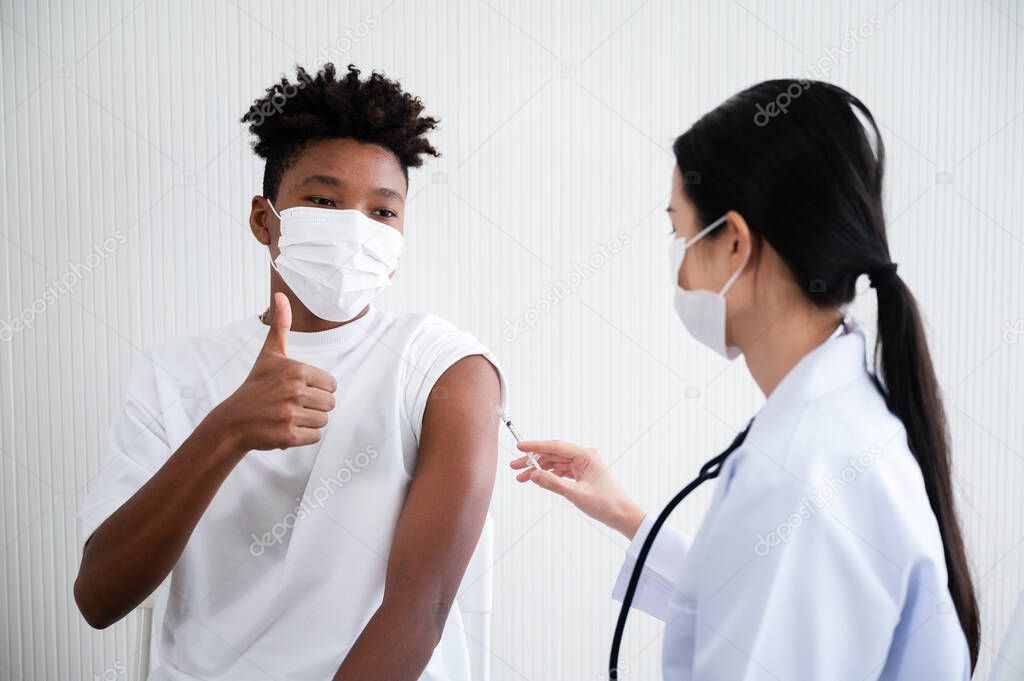 Female doctor or nurse vaccinating against coronavirus 19 at the shoulders African-American man. By wearing a mask at all times. Concept of preventing the spread of COVID-19.