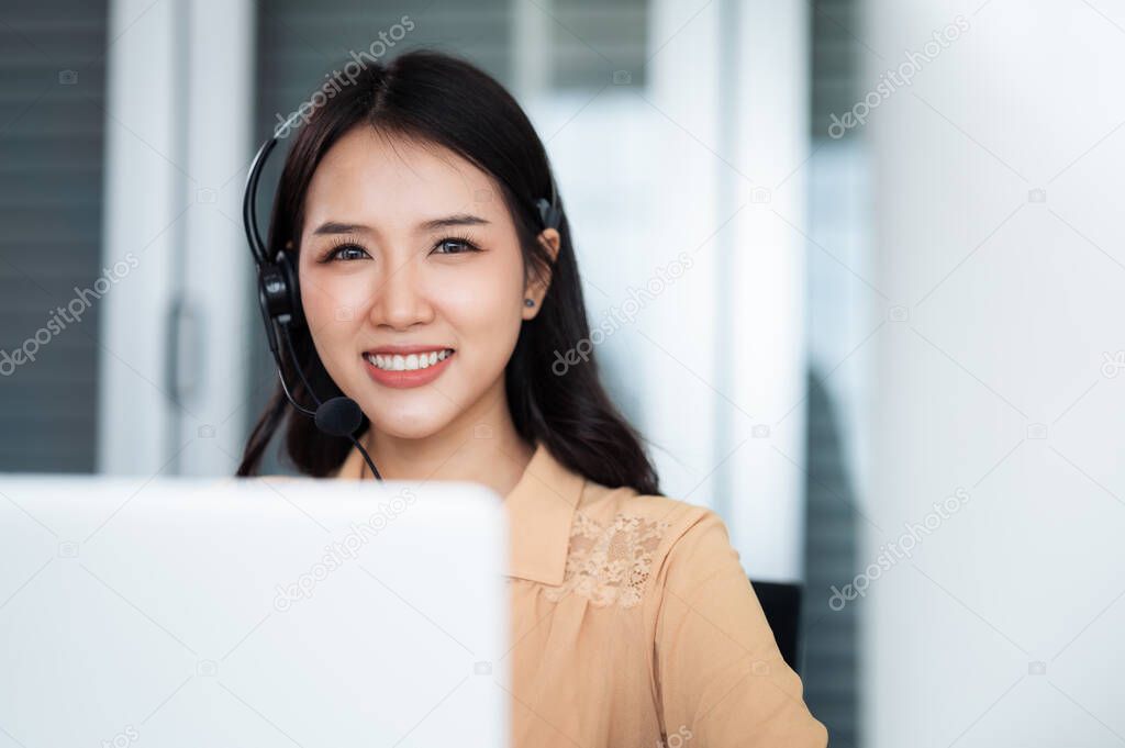 Team of call center staff in Asia wears headphones with a microphone. Smile while serving customers at desks and computers. Service concept and consulting. Communication concept.