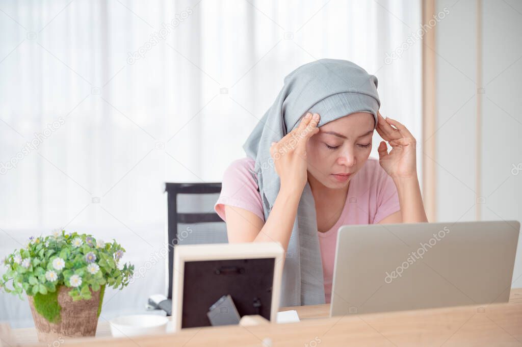 Asian woman wearing a hijab uses her smartphone and laptop in her bed. Attaching a pink ribbon represents recovery from a breast cancer patient. Breast cancer concept, cancer prevention concept.