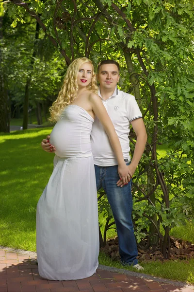 Happy and young pregnant couple in park in summer — Stock Photo, Image