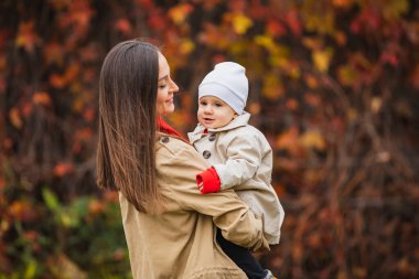 Annemle birlikte sonbahar parkında. Anne ve kızı sonbaharda. Anne bebeği kollarında tutuyor. Anne ve küçük kızı sonbahar parkında yürüyüşe çıktılar. Sonbahar Aile Yürüyüşü.