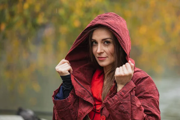 Portrait of a woman in hooded red raincoat walking in park on a rainy autumn day