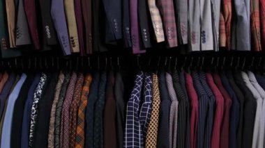 Alışveriş merkezindeki giyim mağazasında sıralanmış askılarda erkek giyim tarzı farklı takımlar var. Mağazada bir sürü kostüm var. İş ve perakende kavramı.