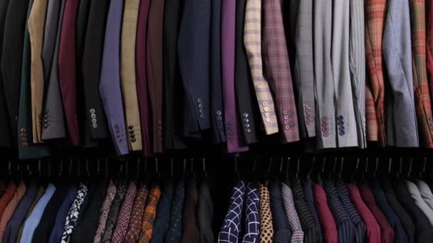 Roupa masculina ternos diferentes clássicos em cabides sucessivamente na loja de roupa no shopping. Muitas fantasias em prateleiras na loja. Conceito de negócio e varejo. — Vídeo de Stock