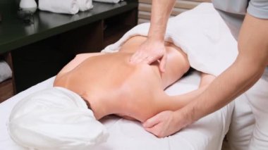 Masör sırt masajı yapıyor. Kaplıca salonunda masaj yaptıran genç bir kadın. Sırt masajı sırasında yavaşça masaj masasında uzanan bir kadının yakın çekimi. 4k