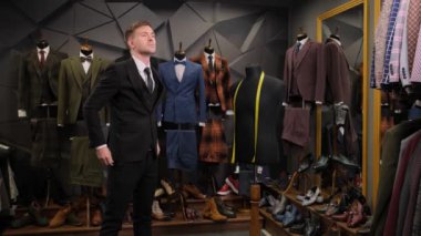 Bir adam lüks bir butik dükkanında aynanın önünde kravatını düzeltiyor. Siyah takım elbiseli bir adamın portresi takım elbiseler, ayakkabılar ve bir mankene karşı..