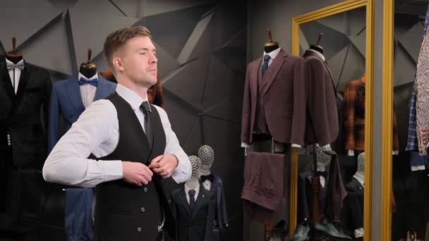 男がベストを着た ビジネスマンは鏡に映る姿を見ている ビジネスマンは スーツ マネキンを背景に高級メンズ衣料品店の鏡を見ています — ストック動画