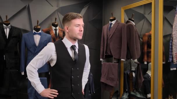 一个男人穿上背心 商人在镜子里看着镜子里的倒影 商人以西装 鞋子和模特为背景 在一家奢侈品男装商店的镜子里照镜子 — 图库视频影像