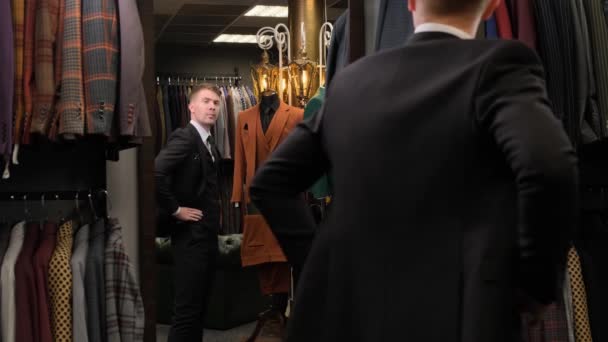 一名男子站在镜子前 靠着模特的背影 伸直袖子 在一家奢侈品服装店扣上夹克时被枪杀 — 图库视频影像