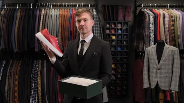 一个商人从一家男装商店的盒子里拿出一只红鞋 背景是服装和一个人体模特 男人穿鞋子 — 图库视频影像