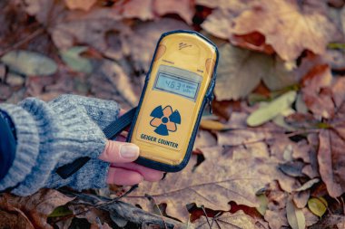dosimeter in a female hand on a background of fallen leaves. Checking radiation level with a personal dosimeter. Pripyat city in Chernobyl Exclusion Zone, Ukraine clipart