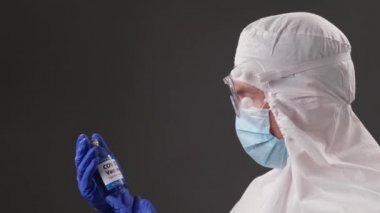Coronavirus aşısının geliştiricisi şeffaf ampul tutuyor. Doktor koruyucu giysi giyiyor. Doktor yeni aşıya bakıyor. COVID Pandemisi 19
