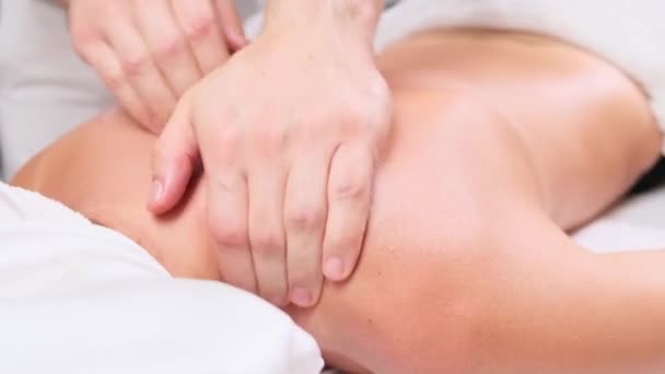 Hombre terapeuta haciendo masaje a paciente mujer acostada en sofá en el gabinete de spa. Cliente femenino recuperando masaje procedimiento rejuvenecedor en clínica de belleza. masaje de hombros y cuello. — Vídeos de Stock
