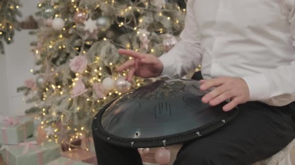 Ein Mann spielt im weihnachtlich dekorierten Raum. Musiker spielt auf der Panzertrommel. Musiker spielt Handpfanne. Musiker spielt auf der stählernen Zungentrommel — Stockvideo