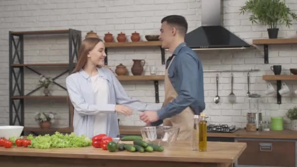 Mladý pár v lásce muž a žena v kuchyni vaření spolu a objímání — Stock video