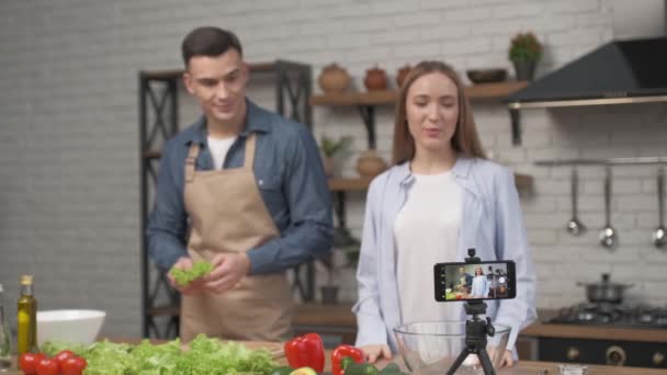 Pareja joven cocinando juntos y grabando video blog de comida en cámara en la cocina en casa — Vídeos de Stock