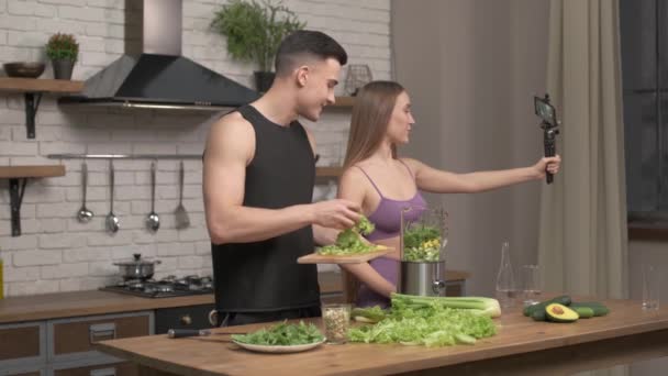 Amante pareja de atletas grabando video comida vlog acerca de la cocina saludable en la cámara del teléfono en la cocina en casa. Vlogging, educación y concepto de redes sociales — Vídeos de Stock