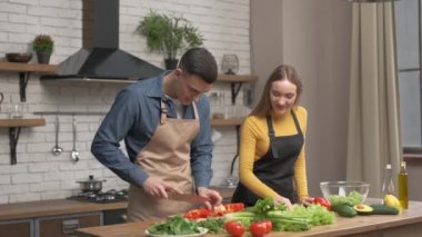 Mutlu çift evde birlikte yemek pişirmekten zevk alıyor. Adam biberleri kesiyor ve kadın gözlüklerle parçaları gözlerine bastırıyor.