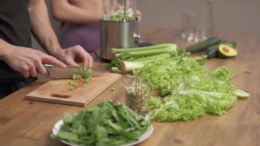 Adam yeşil sebze suyu yapmak için malzemeleri kesiyor. Kadın onu yarı yolda bırakıyor. sağlıklı gıda konsepti