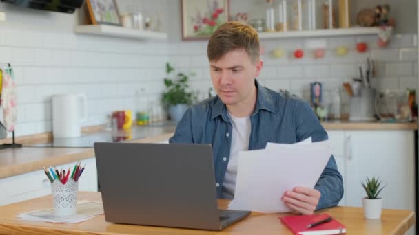 Unge Man Läsa Papper När Använder Laptop Hemma Fokuserad Tusenårig — Stockvideo