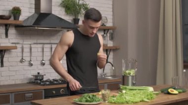 Sporcu modern bir mutfakta smoothie için malzeme hazırlıyor. Blender 'da detoks için sebze hazırlığı. Arka planda avokado, kereviz, salatalık sıvılaştırıcı gümüş kap. Tam HD