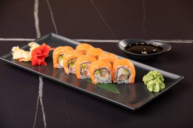 Somon balıklı suşi rulosu ve siyah arkaplanda karides tempurası. Restoran servisi