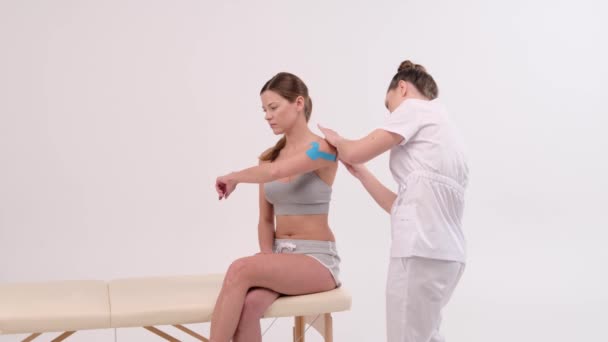 Terapeuta nakłada taśmę kinezjologiczną na kobiece ciało. Koncepcje fizjoterapii i kinezjologii. — Wideo stockowe