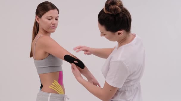 A female physiotherapist is measuring a piece of kinesiotape to be applied on a shoulder joint. He folds a hand in the elbow to check — Stock Video