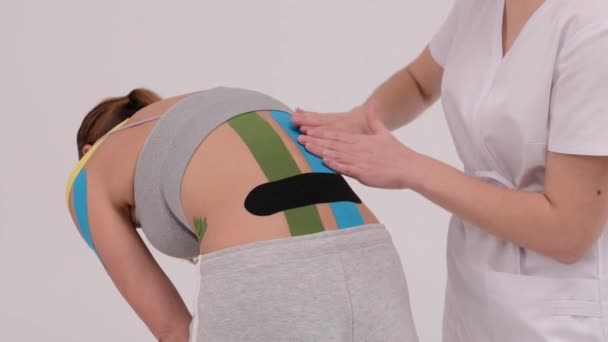 여성 환자 의등에 키 네 시 오 테이프를 녹화하는 치료사의 영상 이 있습니다. 통증 치료. 스포츠와 재활 — 비디오
