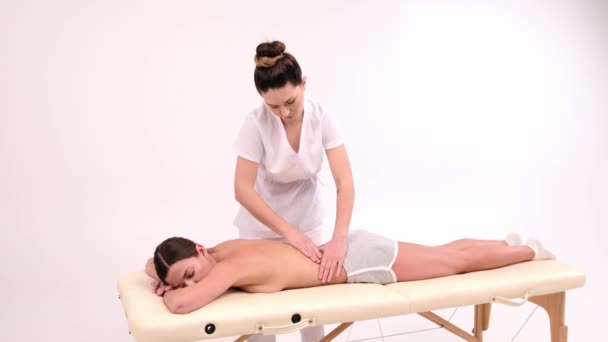 Jovem mulher fazendo massagem no salão de spa. Close-up da mulher relaxante durante a massagem nas costas deitado na mesa de massagem em câmera lenta. — Vídeo de Stock