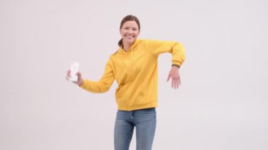 Mutlu genç kadın dans ediyor ve arka planda gülümsüyor. Elinde telefon olan pozitif kız. Komik dans.