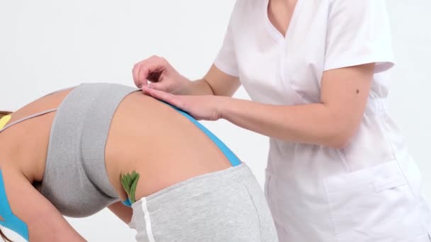 理疗师将运动学磁带贴在女病人的后背 运动学记录 运动学治疗 运动员在腰部受伤后正在康复 沿着脊柱的专业胶水带 — 图库视频影像