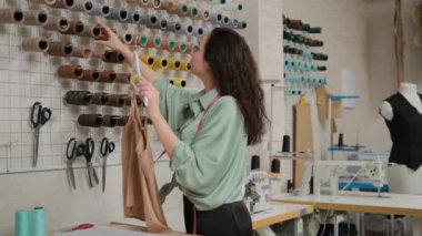 Konsantre kadın postaları terzisi atölyedeki kumaş rengi altında iplikleri topluyor. Yaratıcı çalışma süreci kavramı. Küçük işletme moda tasarımcısı kavramı
