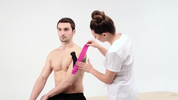 De arts lijmt een speciale behandeling tape om schouder post. Fysiotherapeut plakt kinesio tapes op de schouder van de patiënt, kinesiologie tape, kinesiologische therapie, atleet zijn herstellen na — Stockvideo