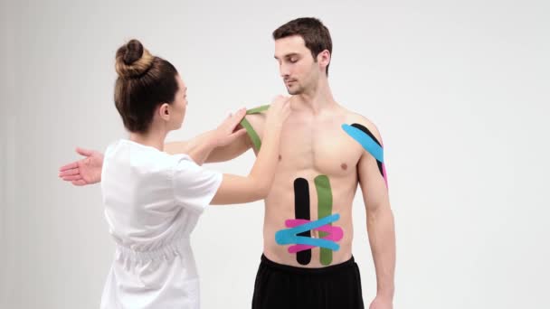 Doktor omzuna özel bir tedavi bandı yapıştırıyor. Fizyoterapist hastanın omzuna Kinesio bantları yapıştırıyor, kineziyoloji bantları, kineziyoloji terapisi, atlet iyileşme sürecinde. — Stok video