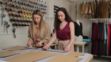 Masada tebeşir ve bezle çalışan iki terzi. Kadın terzi atölyedeki tekstil deseninde tebeşir kullanıyor. Profesyonel terzi, dikiş stüdyosunda moda tasarımcısı..