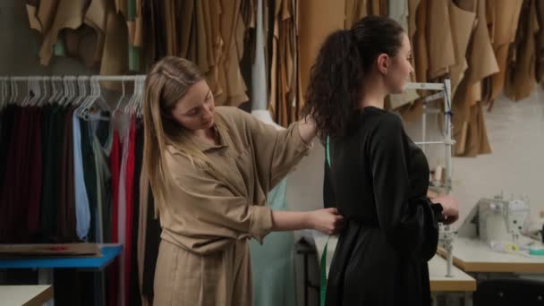 女裁缝用胶带在工作室里测量女客户的尺寸。两个女人在裁缝店一起工作服装的设计师和模特预告片展示了服装尺寸. — 图库视频影像