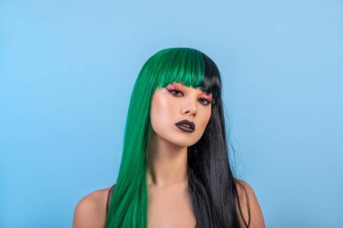 Yeşil siyah peruk takan genç bir kadının güzel portresi, siyah dudak makyajı, temiz ten. mavi arka plan.