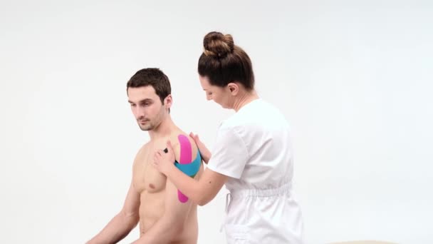 방향타 테이프로 어깨 치료를 했어. 환자의 어깨 부상에 탄성 치료 테이프를 사용하는 물리 치료사 — 비디오