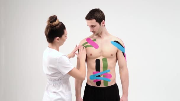 Schouderbehandeling met kinesio tape. Fysiotherapeut die elastische therapeutische tape op schouderletsel van de patiënt aanbrengt — Stockvideo